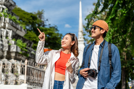 Young Asian couple man and woman traveling backpacker walking in temple at Bangkok Thailand. Happy couple tourist walking in the downtown street. Holiday vacation time touristの写真素材