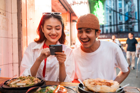 Asian couple man and woman enjoy eating street food noodle at night market. Traveler Asian couple blogger Happy tourists with Traditional food local road at thailand bangkok city.の写真素材