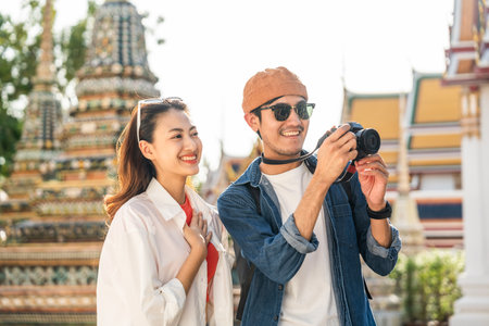 Young Asian couple man and woman traveling backpacker walking in temple at Bangkok Thailand. Happy couple tourist walking in the downtown street. Holiday vacation time touristの写真素材