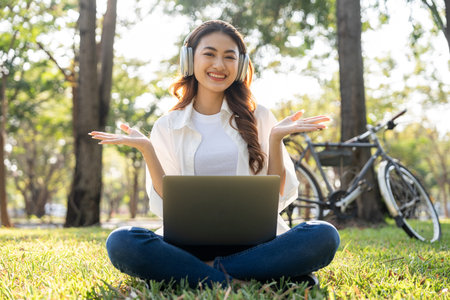 Young asian teenager learning with laptop sitting in the public park. Summer time spring young women working outdoors living in nature. Human and nature togetherの写真素材