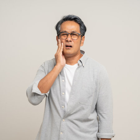 Old man senior puts his hand on his mouth and feels toothache because of tooth decay. Problems with teeth bad breath. Mature man unwell unhealthy standing on isolated backgroundの写真素材