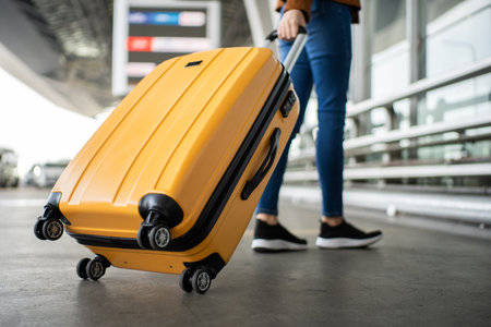 Close up of unrecognized woman tourist walking with her luggage through international airport terminal during holiday trip, female tourist rolling suitcase alone.の写真素材