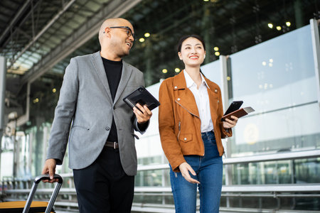 Portrait of confident young business people smiling at camera and traveling with luggage and passport with ticket boarding pass while standing in the international airport terminal.の写真素材