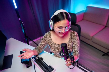 Content creator woman host streaming her a podcast with headphones and microphone interview cheering guest conversation broadcast studio with neon light. Blogger motivation recording voice over radioの写真素材