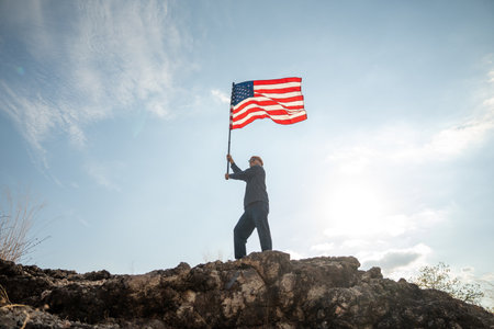 Portrait of cheerful young man looking forward while standing proudly with holding USA flag over his...