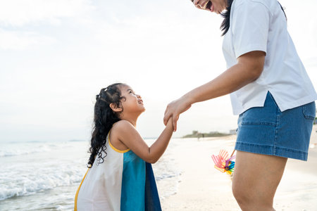 Happy young asian mother and her child walking and holding hands on the beach and enjoy a sunset by the ocean. mom and cheerful kid girl having fun and relaxation on a tropical seaside vacation.の写真素材