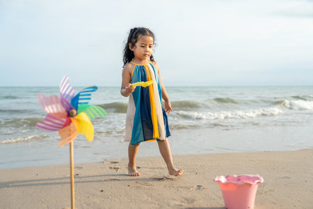 Cheerful adorable little girl having fun outdoor and playing with sand with beach kid toys on the...
