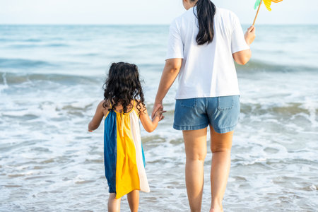Happy young asian mother and her child walking and holding hands on the beach and enjoy a sunset by the ocean. mom and cheerful kid girl having fun and relaxation on a tropical seaside vacation.の写真素材