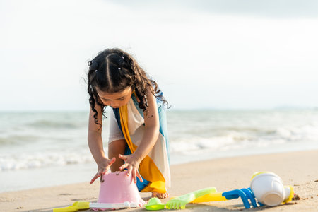 Cheerful adorable little girl having fun outdoor and playing with sand with beach kid toys on the beach in the summer vacation at sunset, happy healthy toddler playful on the tropical seaside.の写真素材