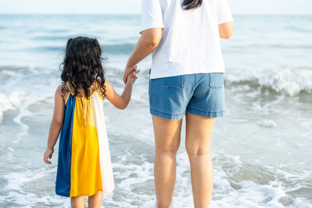 Happy young asian mother and her child walking and holding hands on the beach and enjoy a sunset by the ocean. mom and cheerful kid girl having fun and relaxation on a tropical seaside vacation.の写真素材