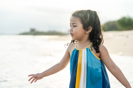 Cheerful adorable little girl having fun outdoor and playing with sand with beach kid toys on the beach in the summer vacation at sunset, happy healthy toddler playful on the tropical seaside.の写真素材