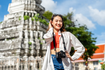 Young Asian woman traveling backpacker walking in temple at Bangkok Thailand. Happy female tourist walking in the downtown street traditional ancient temple. Holiday vacation time touristの写真素材