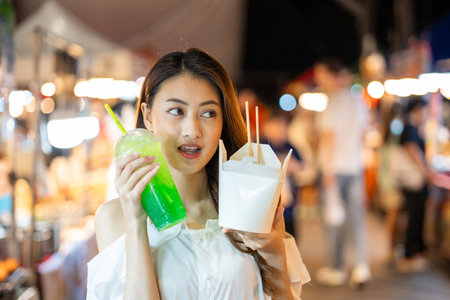 Asian woman enjoy eating noodles street food at night market. Traveler Asian blogger women Happy tourists Beautiful female with Traditional thailand bangkok food.の写真素材