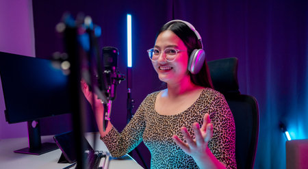 Content creator woman host streaming her a podcast with headphones and microphone interview cheering guest conversation broadcast studio with neon light. Blogger motivation recording voice over radioの写真素材
