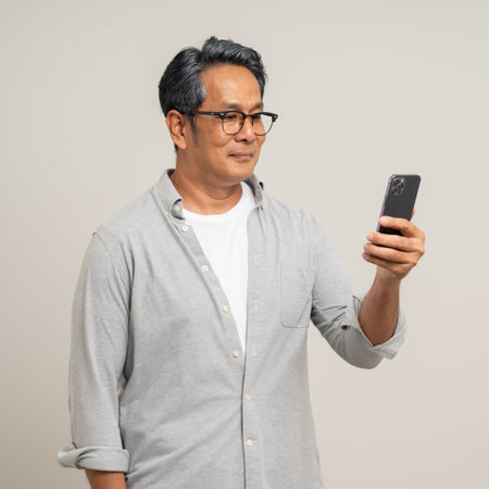 Handsome asian mature old man standing using smartphone on isolated white background. Happy Portrait of cheerful smiling senior asian man holding cell phone. Mature People and lifestyleの写真素材