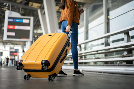 Close up of unrecognized woman tourist walking with her luggage through international airport terminal during holiday trip, female tourist rolling suitcase alone.の写真素材