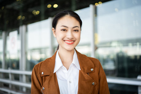 Portrait of confident young businesswoman smiling at camera ready traveling business trip with holding passport with ticket boarding pass and smartphone at the international airport terminal.の写真素材