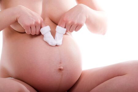 Sitting mother plays with socks on her belly (8th month). Not R-Rated! White background.の写真素材