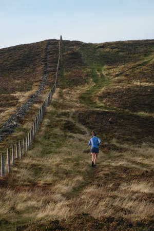 A woman is running among the Scottish hills in the park. The view from the back.の写真素材