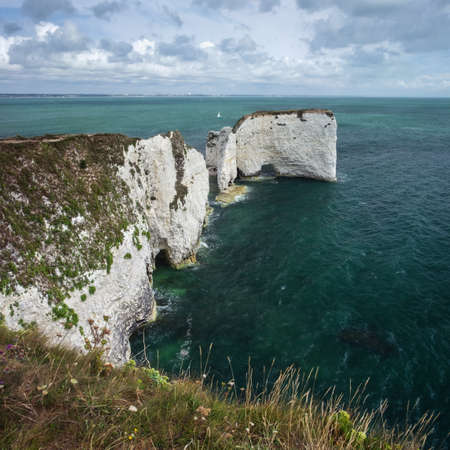 Cliffs on the sea coast and a sailboat. August - 2019. Old Harry Rocks, England