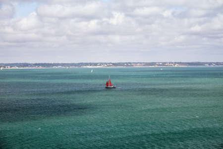 Sailing yacht with red sail goes on the turquoise sea, English Channel, United Kingdomの写真素材