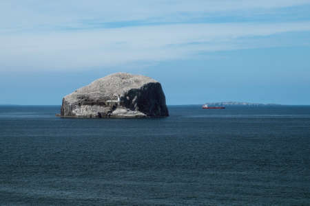 Lighthouse on a cliff, sea, seagulls and red ship. Bass Rock, Scotland, United Kingdomの写真素材