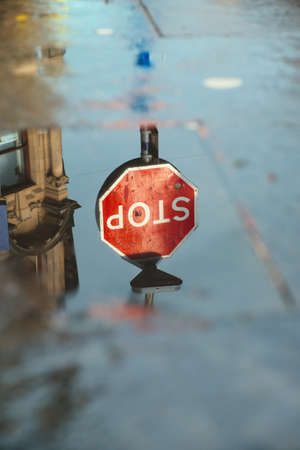 Reflection of the STOP road sign in a puddle after rain on a city street. Dunfermline, United Kingdom. Content does not contain visible brand names or logosの写真素材