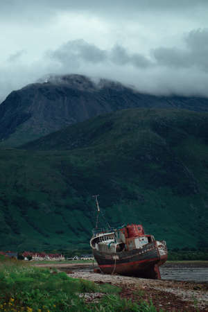 An old ship washed ashore on Loch Linnhe at Fort William on the Highland coast of Scotland. Opposite a high cloud-covered mountain Ben Nevisの写真素材