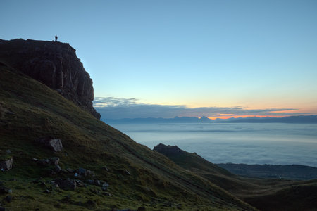 Silhouette of a traveler standing on a large rock and looking at the sea before the rising sun. Isle...