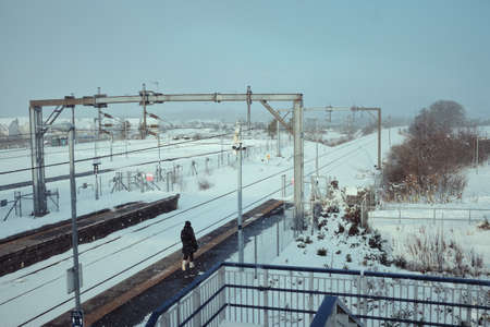 Railway station platform in the snow and a lonely walking passenger. Scotland in winterの写真素材