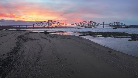 View of Forth Rail Bridge at sunset and the sandy coast in the foreground. Scotland, United Kingdom