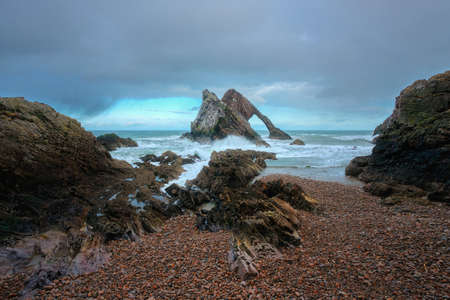 Amazing view of the sea cliffs, in the shape of an arch and stones in the foreground. Famous rock formation on the Moray Coast, Scottish Highlands, Scotland. Bow Fiddle Rock.の写真素材