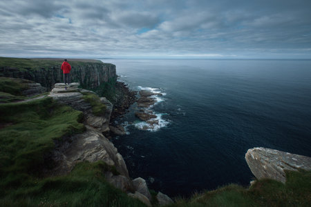 A red-jacketed hiker on top of a cliff looks out over the magnificent scenery of the sea bay. Dunnet Head, Scotlandの写真素材