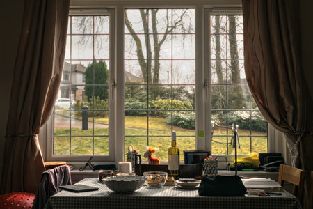 A living room with a table in front of a window overlooking a sunlit lawn. On the table are various household items. Scotland, United Kingdomの写真素材