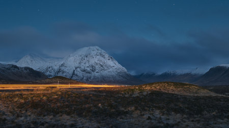 Night view of a road leading through the Scottish Highlands of Glen Coe with car light trail, snowcapped mountains and valley. Scotlandの写真素材