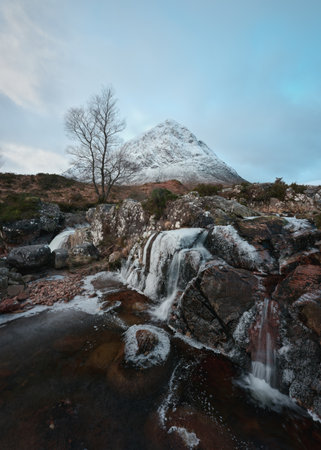 Mountain river and partially frozen waterfall at the foot of the snow-covered Buachaille Etive Mor. Etive Mor Waterfall. At the entrance to the valley of Glencoe in the Scottish Highlands, Scotlandの写真素材