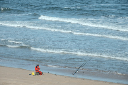 A fisherman with a fishing rod sitting on the seashore. North Sea, Scotlandの写真素材
