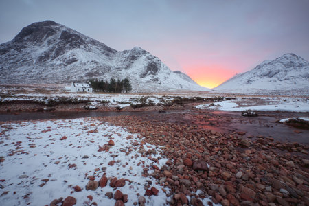 A remote hut and a river with stones on the foreground at the foot of Buachaille Etive Mor at the entrance to the valley of Glencoe in the Scottish Highlands, Scotlandの写真素材
