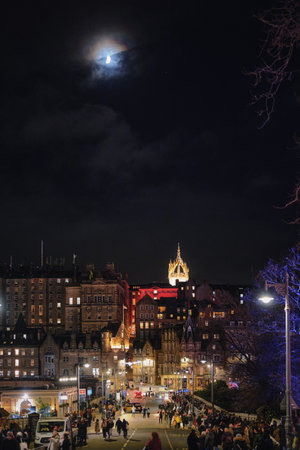 Night view of central Edinburgh, Scotland, on 8 December 2024. People walking under moonlit sky with illuminated historic buildings and St. Giles Cathedral tower.のeditorial素材