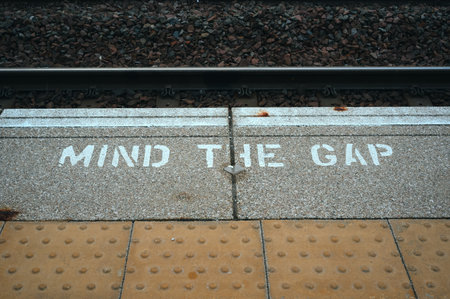 Close-up of Mind the Gap warning text on a train station platform near railway tracks. Travel safety reminder in the UK transportation system.の写真素材