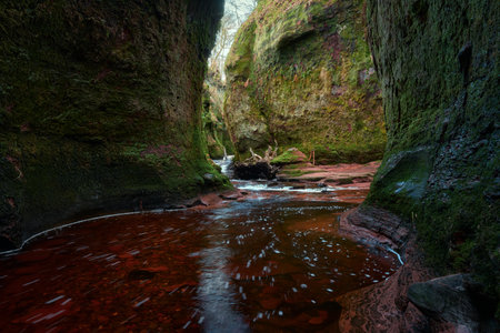 Scenic view of Finnich Glen in Scotland with moss-covered rock walls, flowing river and vibrant red sandstone. Atmospheric natural landscape and unique geological formation.の写真素材