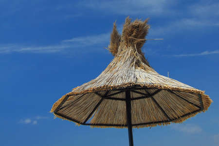 Straw sun umbrella, parasol on a sunny blue skyの写真素材