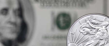 Silver shiny dollar coin on a background of blurry one hundred dollar billの写真素材