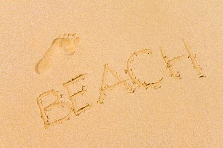 Footprint and the word beach written with the finger in the sandの写真素材