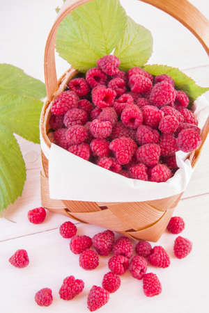 Fresh fruits raspberries in a wooden little punnet on a white table