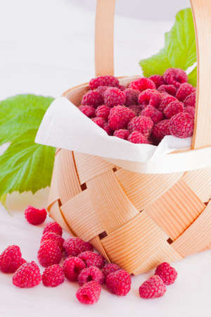 Fresh fruits raspberries in a wooden little basket on a white table