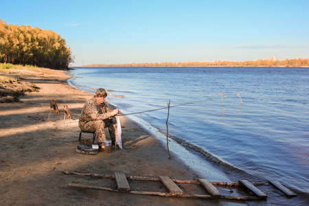 A fisherman on the river bank is closely monitoring the fishing rodの写真素材