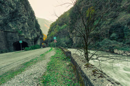The mountain river flows near the mountain road leading to the tunnelの写真素材