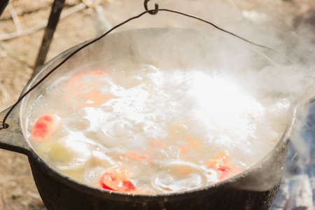 A pot with fish soup cooked on a tripod over a fireの写真素材