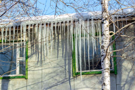 Icicles hanging from a wooden house roofの写真素材